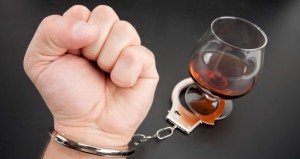 A hand locked to glass of alcohol by handcuffs